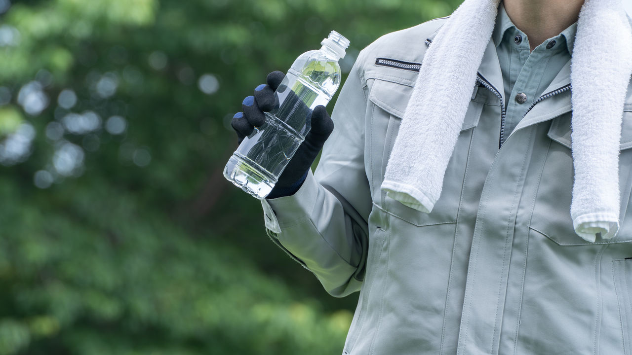 プラスチックボトルの水を飲む作業服の男性|建設業の熱中症対策イメージ