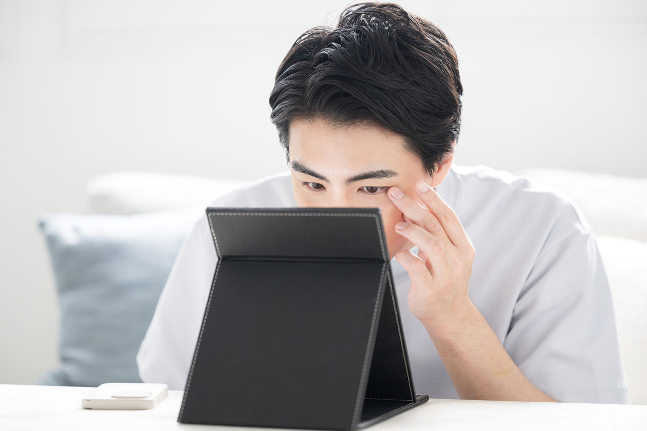 部屋で鏡を見ながらコンタクトなどを入れる男性のクローズアップ 目の渇きでドライアイや充血