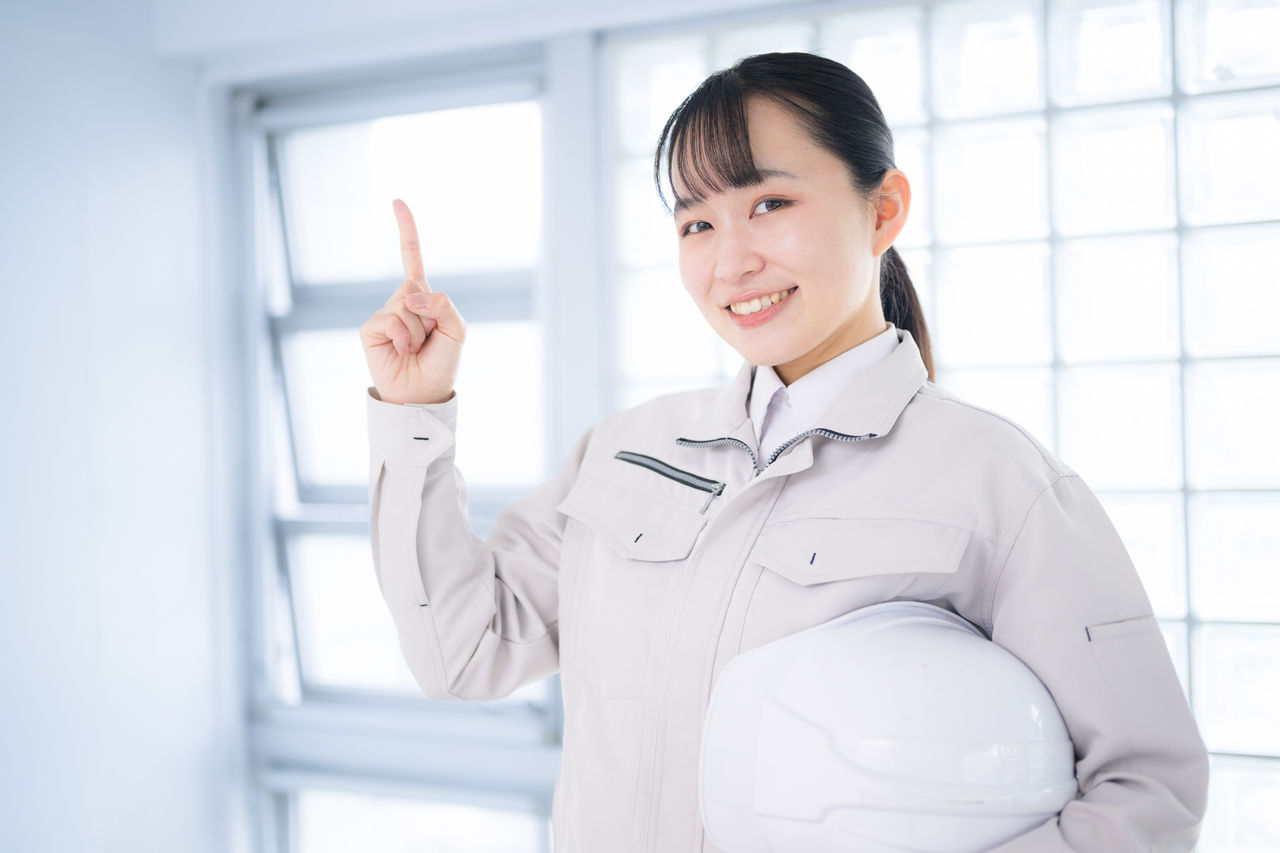 作業着を着たカメラ目線の女性　指さしでオススメやポイント