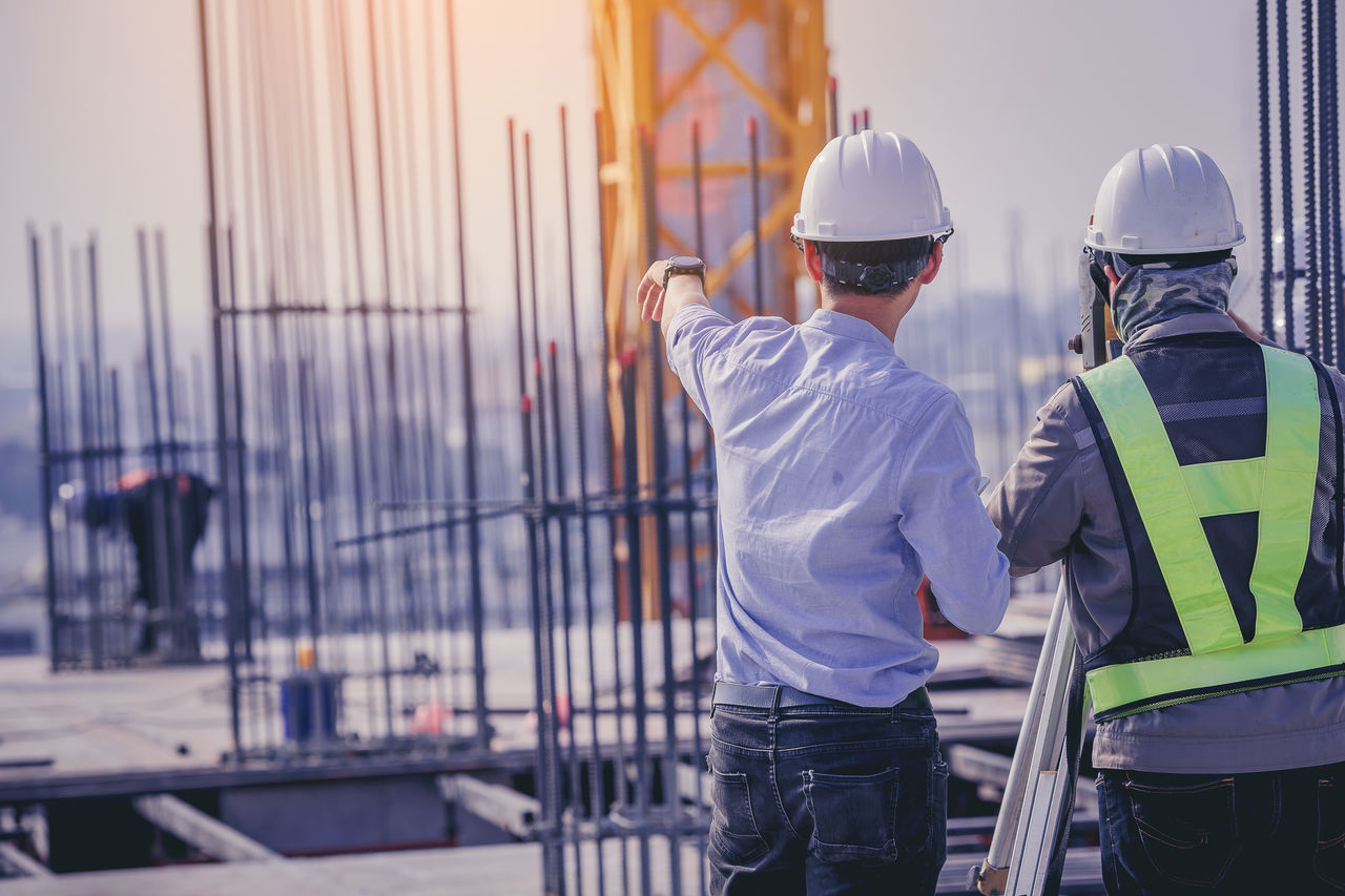Engineer and worker working with theodolite transit equipment at outdoors construction site.